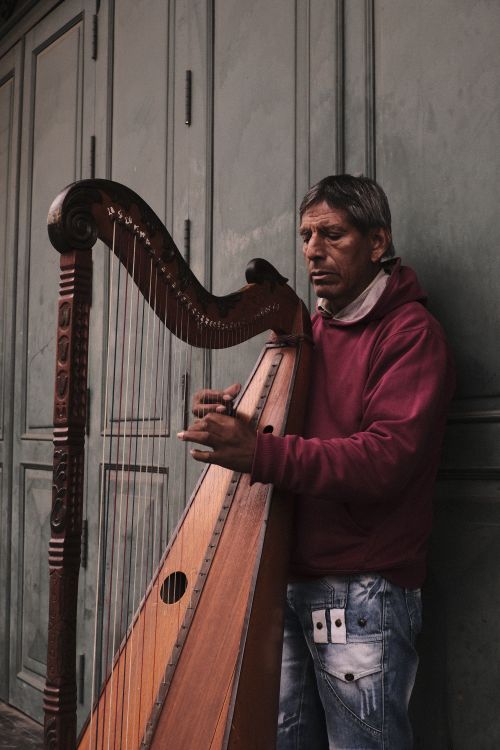 Free A street musician plays a classic wooden harp outdoors, adding charm to the urban setting. Stock Photo