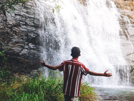 A man with arms outstretched stands near a waterfall, enjoying the serenity.