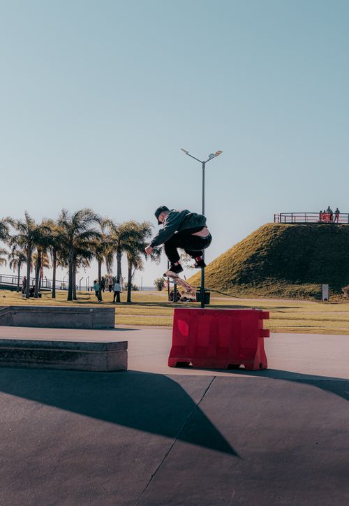 Free Skateboarder mid-air during a trick at an outdoor skate park on a sunny day. Stock Photo