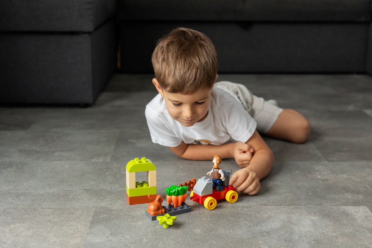 A young boy playing with colorful toy blocks on the floor near rolling under-bed LEGO storage