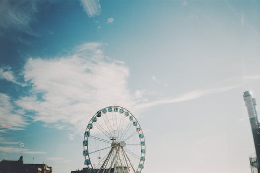 A large ferris wheel set against a bright blue sky with clouds in Helsinki, Finland. by Inga Seliverstova