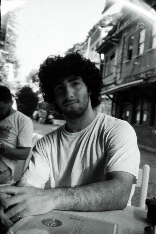 Free Black and white portrait of a young man with curly hair sitting at an outdoor cafe. Stock Photo