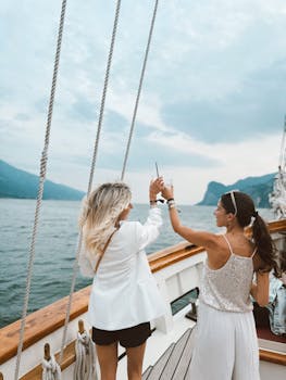 Two stylish women toasting on a yacht cruise in Italy's beautiful lake scenery.