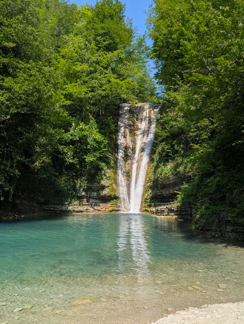 Free Tranquil waterfall surrounded by lush greenery, cascading into a turquoise pool under a clear blue sky. Stock Photo