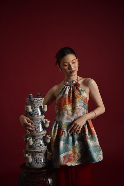 Free Elegant woman in colorful dress posing with intricate ceramic tower against red backdrop. Stock Photo