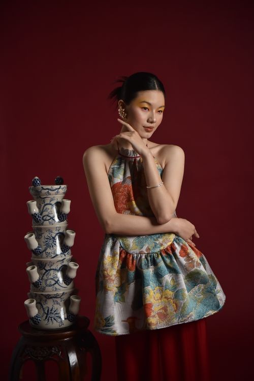 Free Stylish woman in floral attire with stacked blue porcelain against red backdrop. Stock Photo