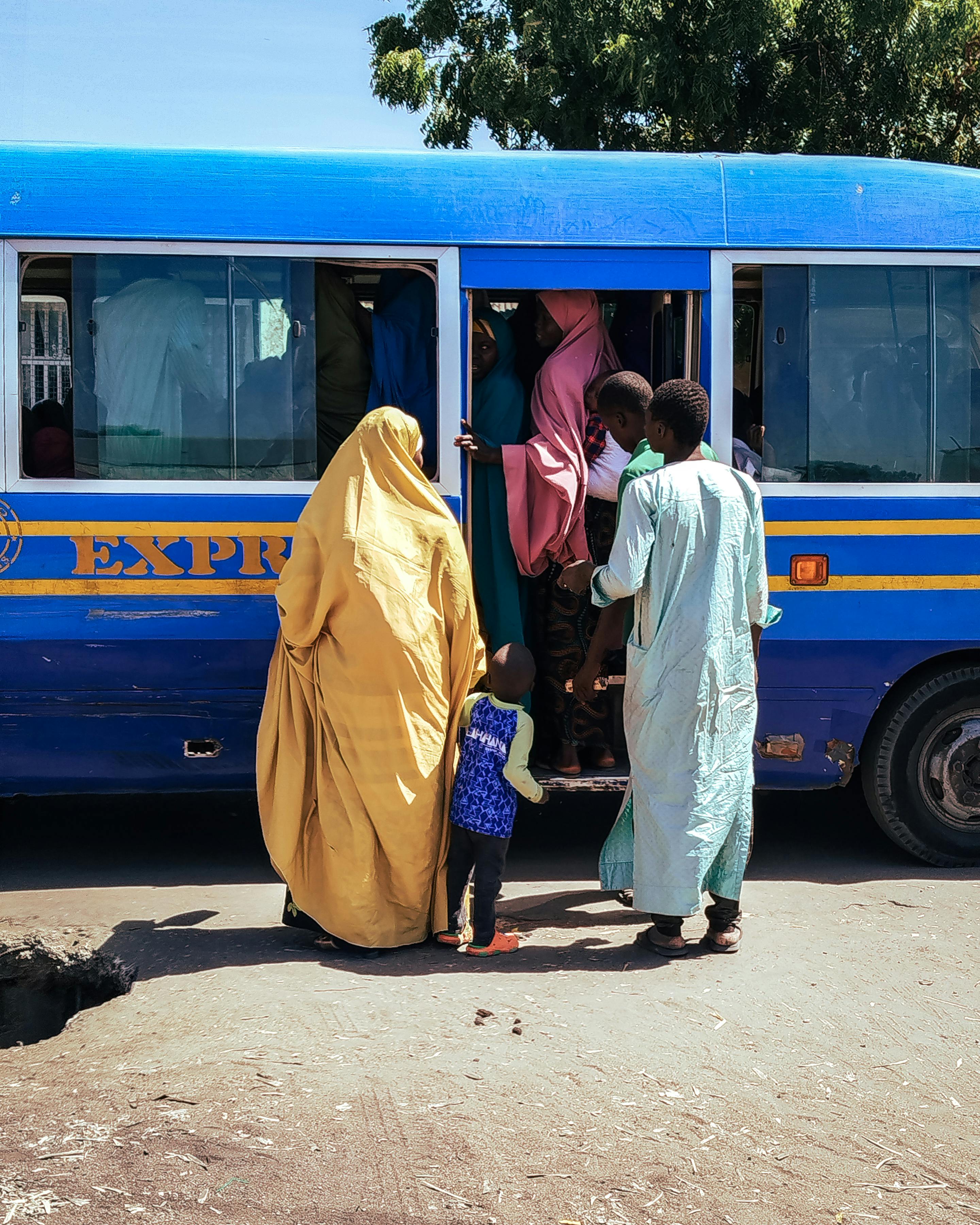 Vibrant street scene at a Nigerian bus stop with people boarding a bus on a sunny day.
