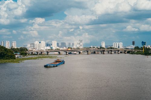 Free A bustling view of the Saigon River with a barge and the city skyline under a blue sky. Stock Photo