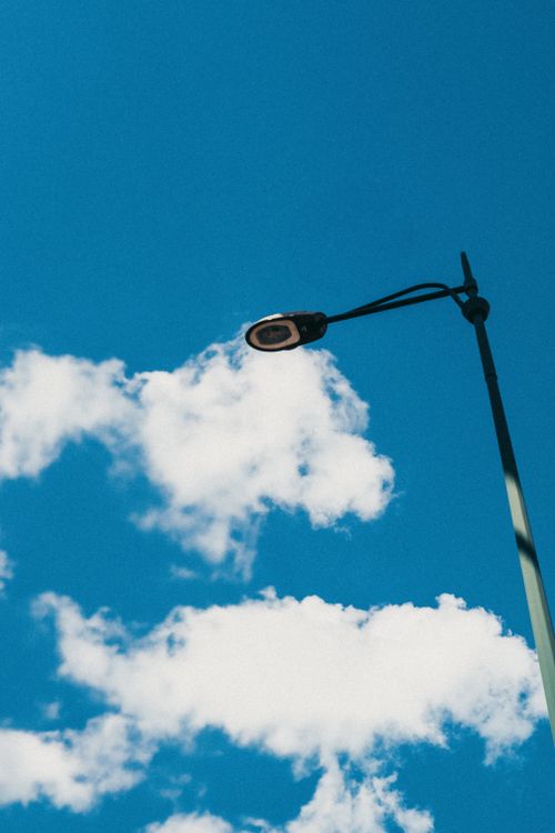 Free Minimalistic view of a street lamp reaching into a clear blue sky with fluffy clouds. Stock Photo
