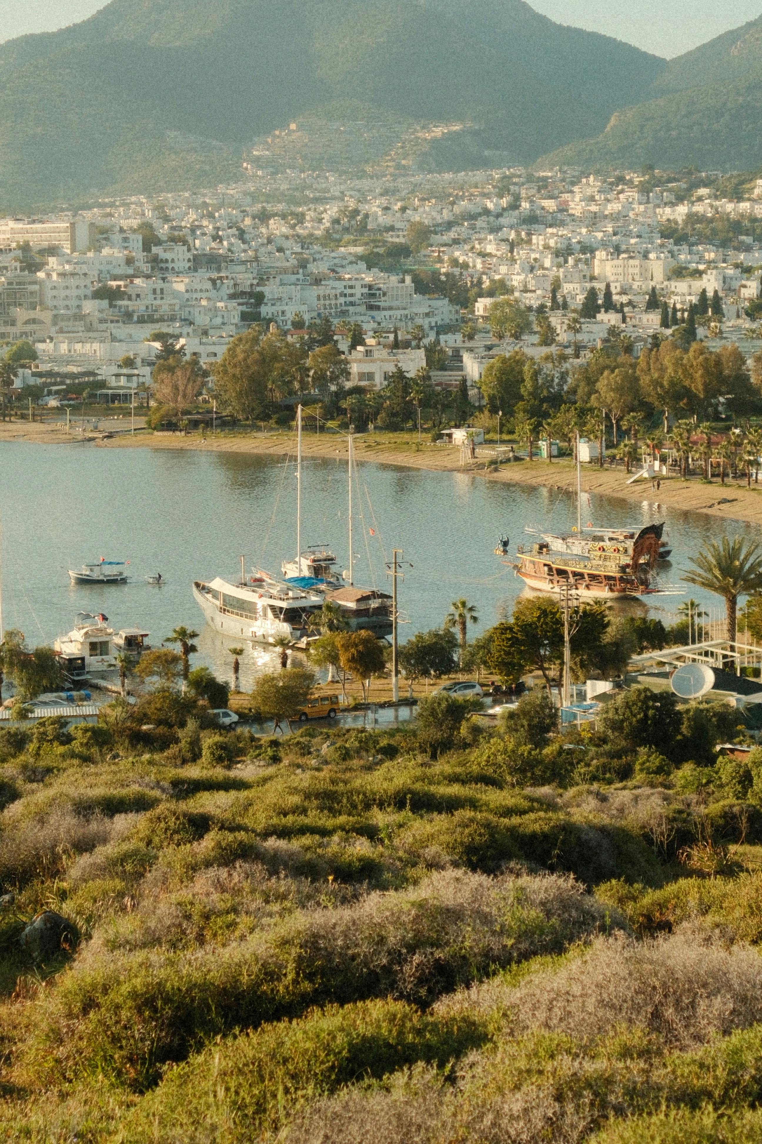 A picturesque harbor with boats, mountains, and a quaint coastal city in view.