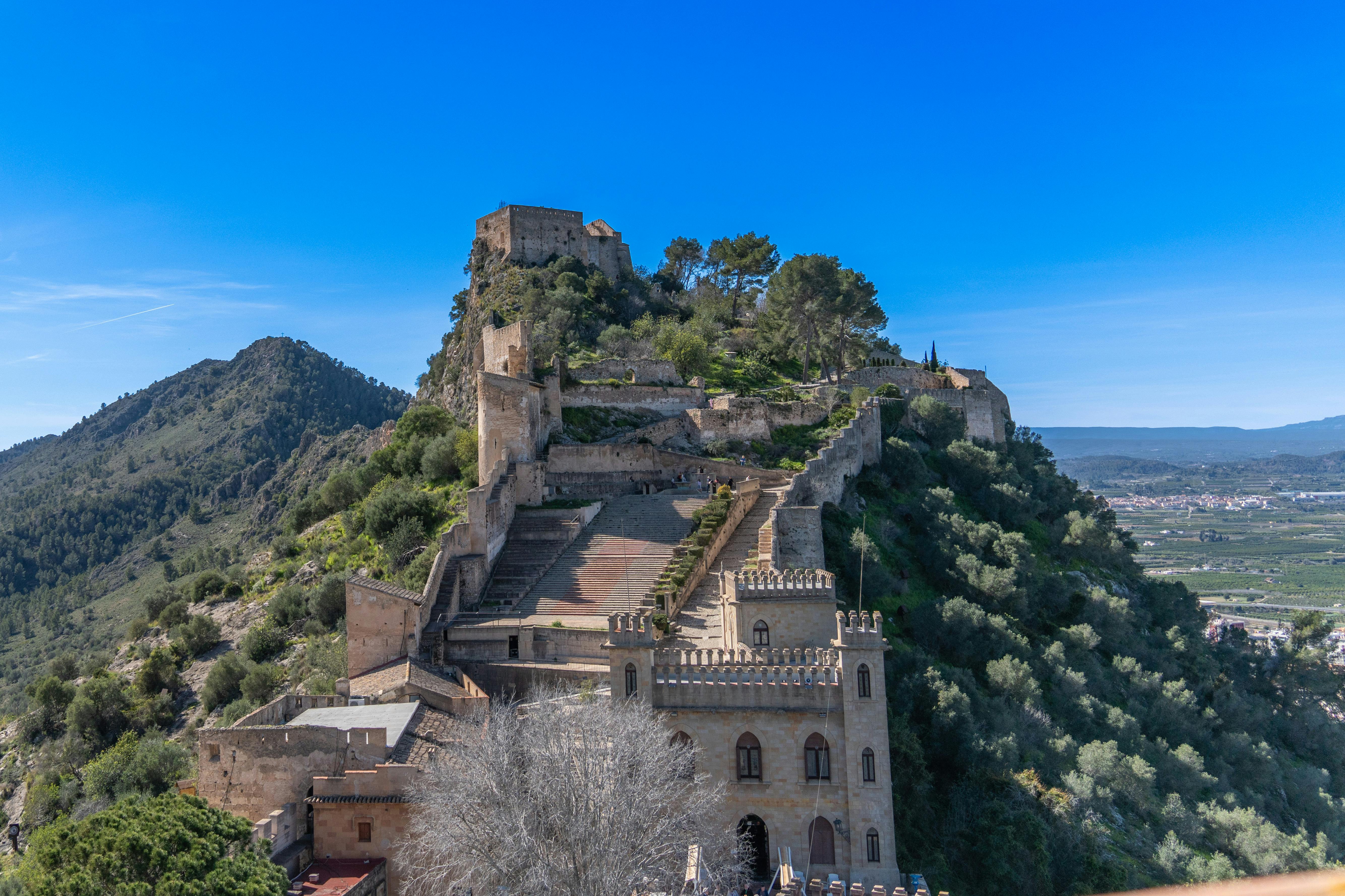 Aerial view of Xàtiva Castle surrounded by lush greenery under a clear blue sky.