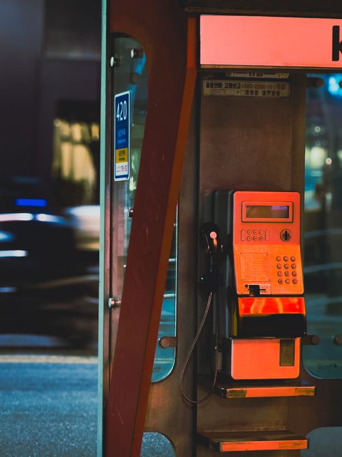 Free A city street corner with a vintage phone booth at night, illuminated by urban lights. Stock Photo