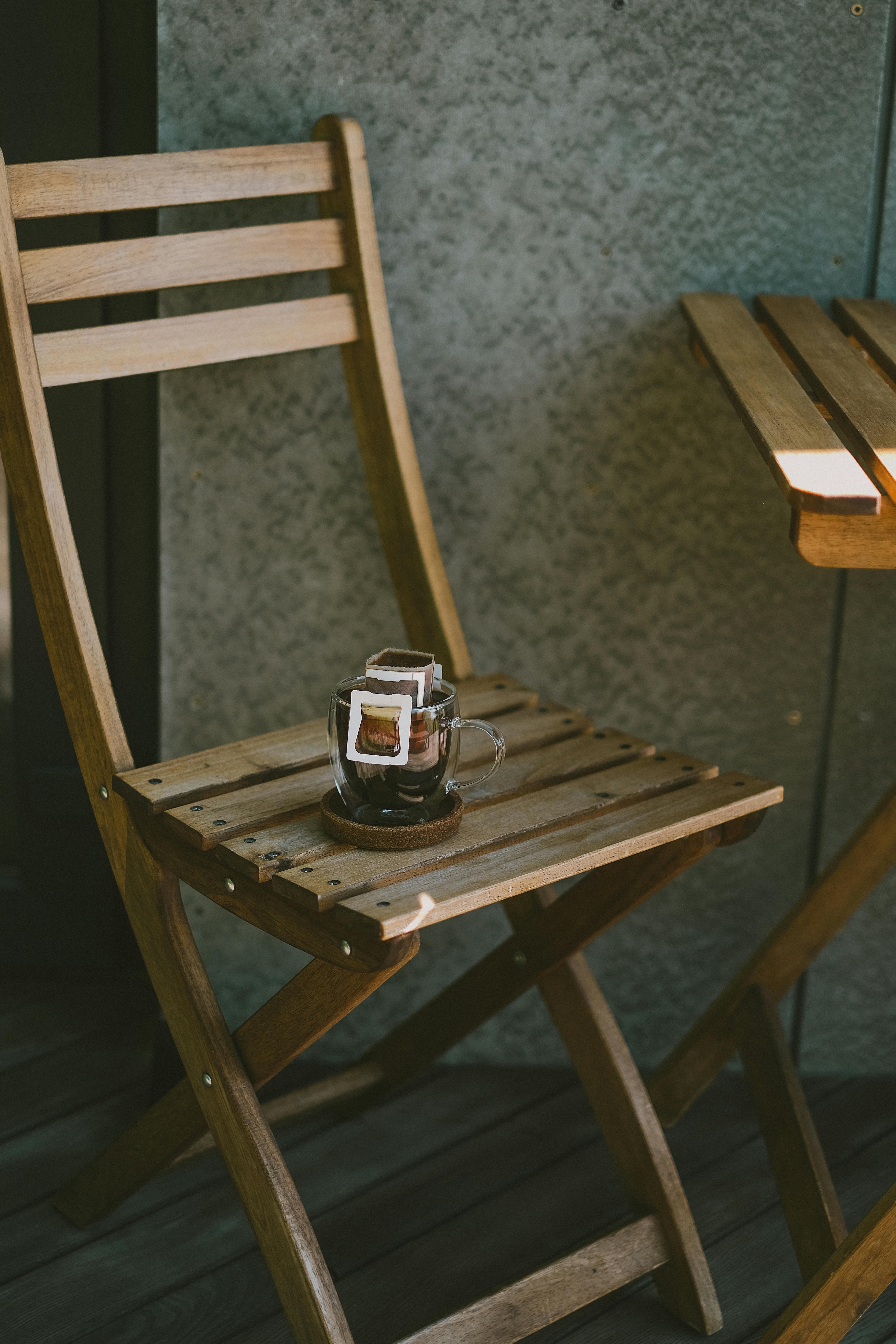 A clear glass cup of drip coffee resting on a wooden chair, creating a cozy outdoor vibe.
