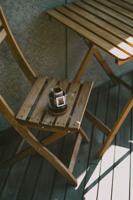 Warm morning coffee on a wooden chair under sunlight exudes a minimalist, peaceful vibe.