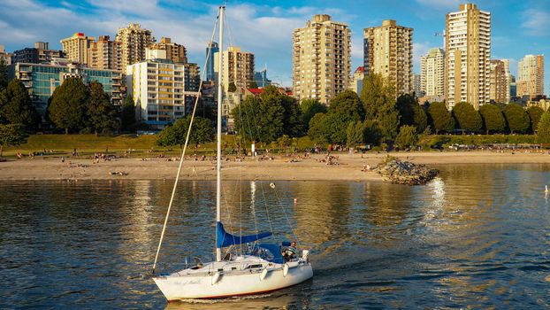Sailboat gracefully gliding on water against urban skyline during beautiful day.