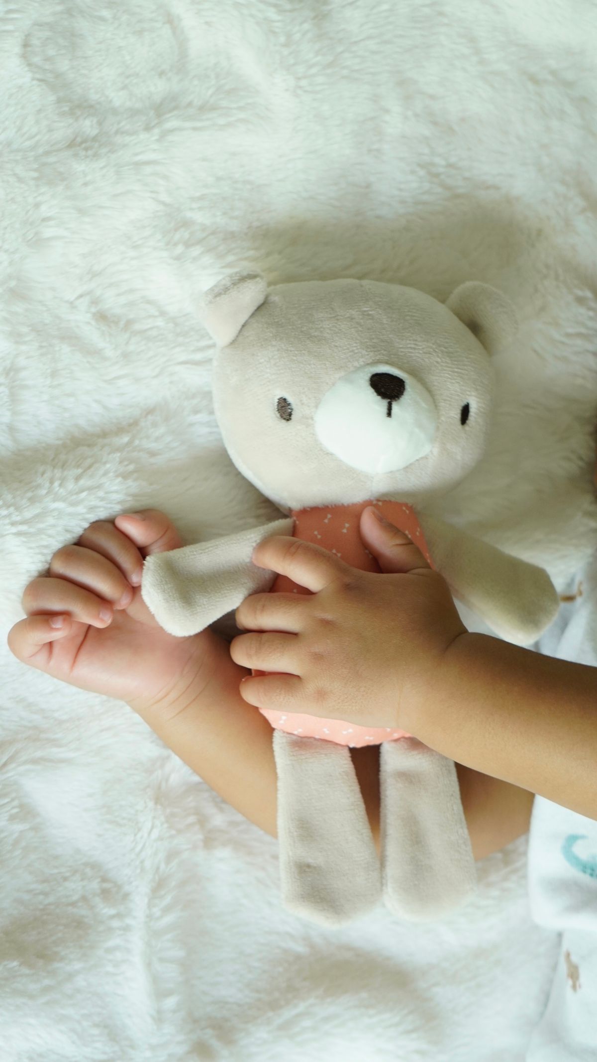 Child holding a soft teddy bear on a blanket