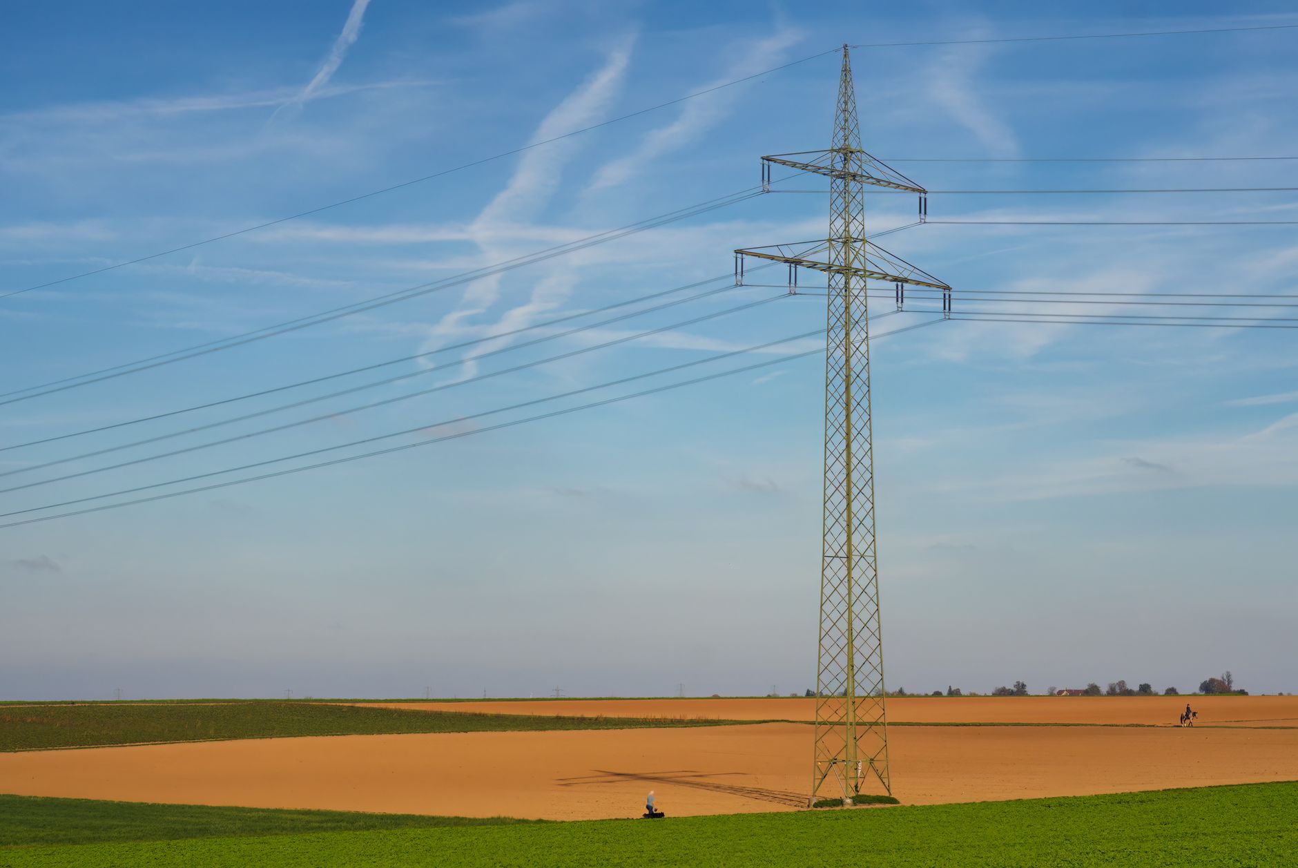 High voltage power line standing tall in a vast agricultural field under a clear blue sky in Germany.