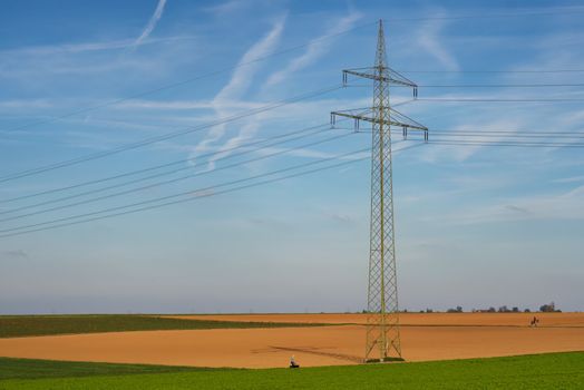 High voltage power line standing tall in a vast agricultural field under a clear blue sky in Germany.