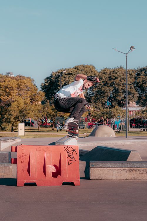 Free Young man executing a skateboard trick at an outdoor urban skatepark with trees and blue sky. Stock Photo