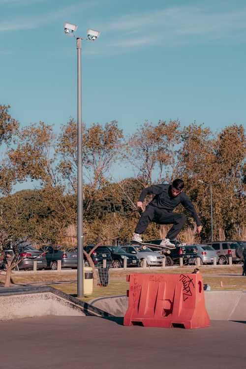 Free A male skateboarder performs a trick over a barrier at an outdoor skate park on a sunny day. Stock Photo