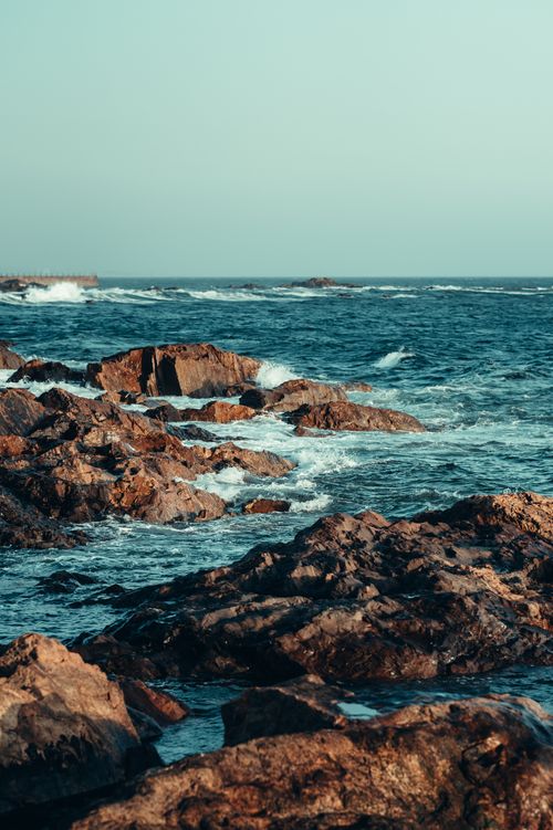 Free Dramatic view of a rocky coastline with waves crashing against the shore under a clear sky. Stock Photo
