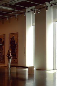 A woman admires paintings in a sunlit art gallery with modern architecture.