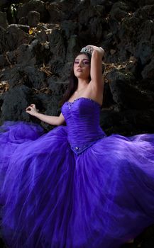 Graceful woman in a stunning purple quinceañera dress posing by rocks.