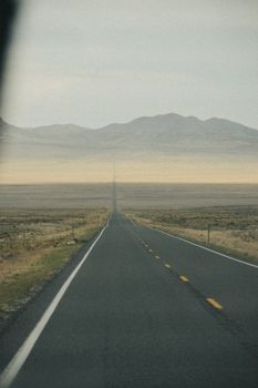 A solitary road stretches through a vast desert towards distant mountains under an overcast sky.