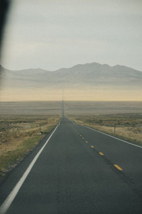 Free A solitary road stretches through a vast desert towards distant mountains under an overcast sky. Stock Photo
