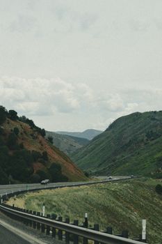 Winding road through lush green mountains with cloudy sky, perfect for travel and adventure themes.