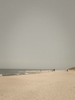 A serene beach scene with a few people walking and enjoying the vast sandy shore.