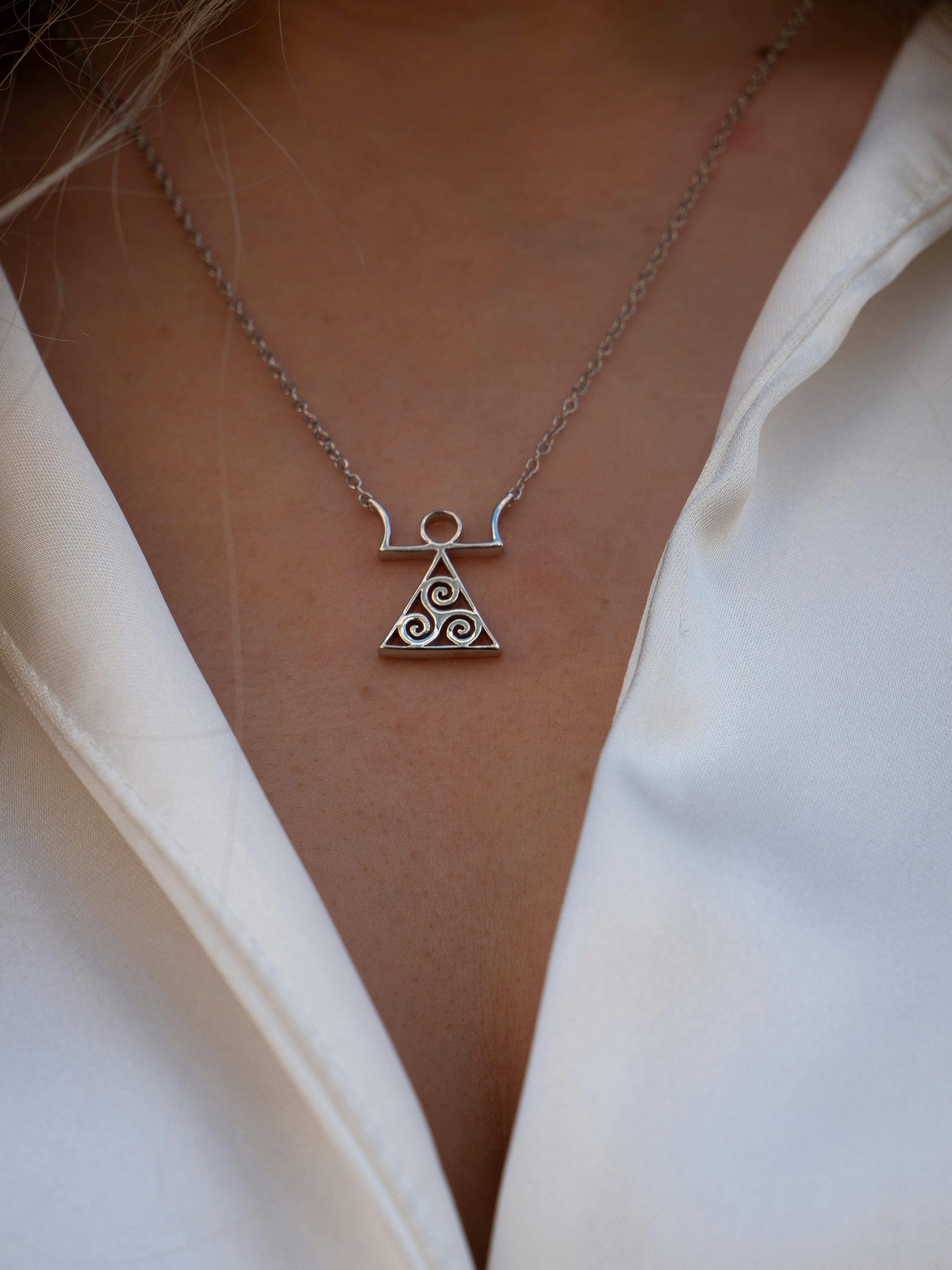 Close-up of an elegant silver triangle pendant necklace on white fabric, highlighting its intricate design.