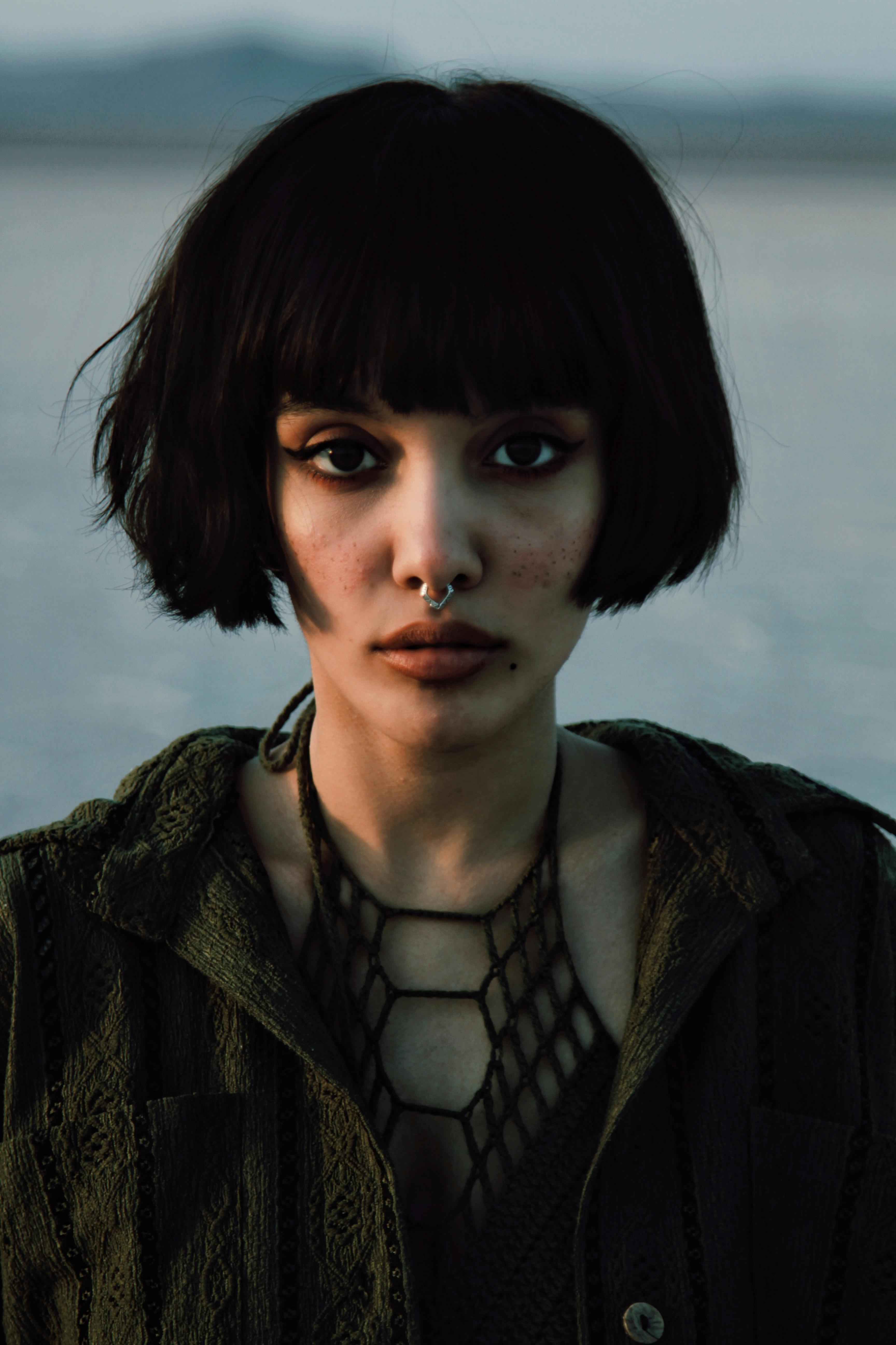 Striking portrait of a young woman with short hair and nose ring in a natural setting.