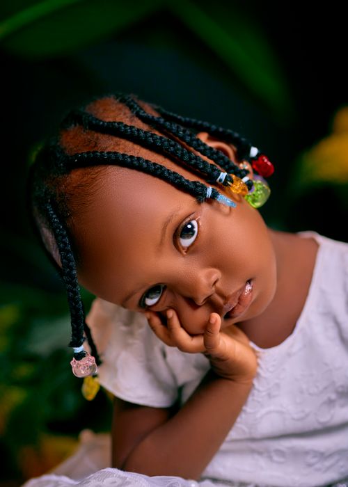 Free Cute African child with braided hair and colorful beads, resting her face on her hand. Stock Photo
