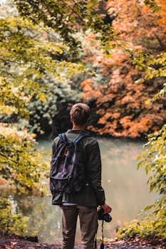 一名背着背包和相机的男子，正享受着秋叶环绕的宁静河景