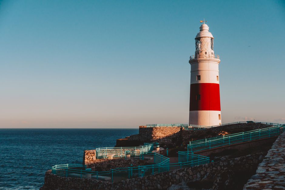 Stark lighthouse at Europa Point, Gibraltar shines brightly against the blue sea in golden hour.