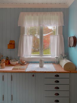 Charming vintage kitchen interior with light blue cabinetry and cozy accents, softly lit by a window.