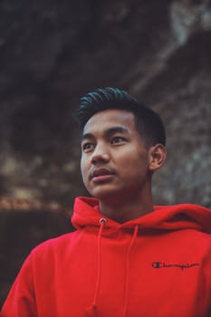 一个穿着红色连帽衫的年轻人若有所思地站在户外