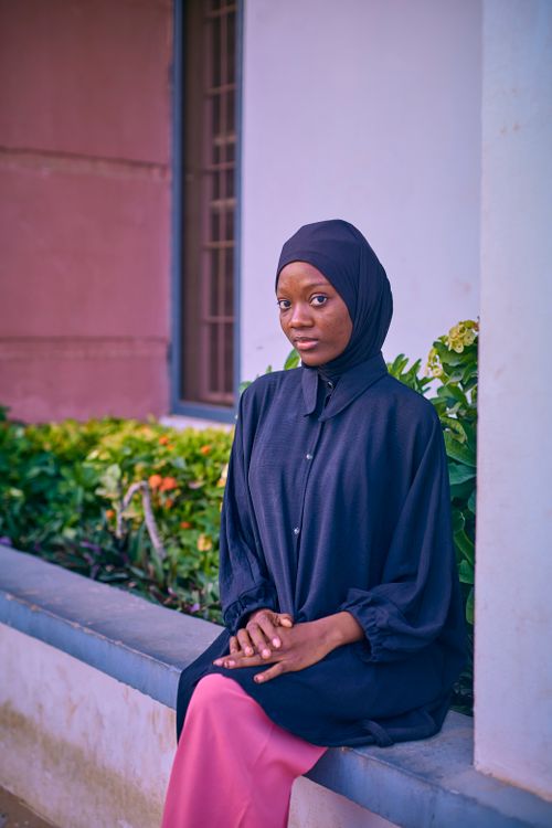 Free Elegant portrait of a woman wearing a hijab, seated casually in an urban setting with greenery. Stock Photo