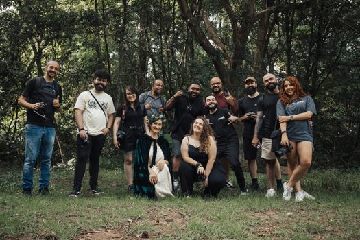 A diverse group of photographers gathered outdoors in a forest, smiling and holding cameras.