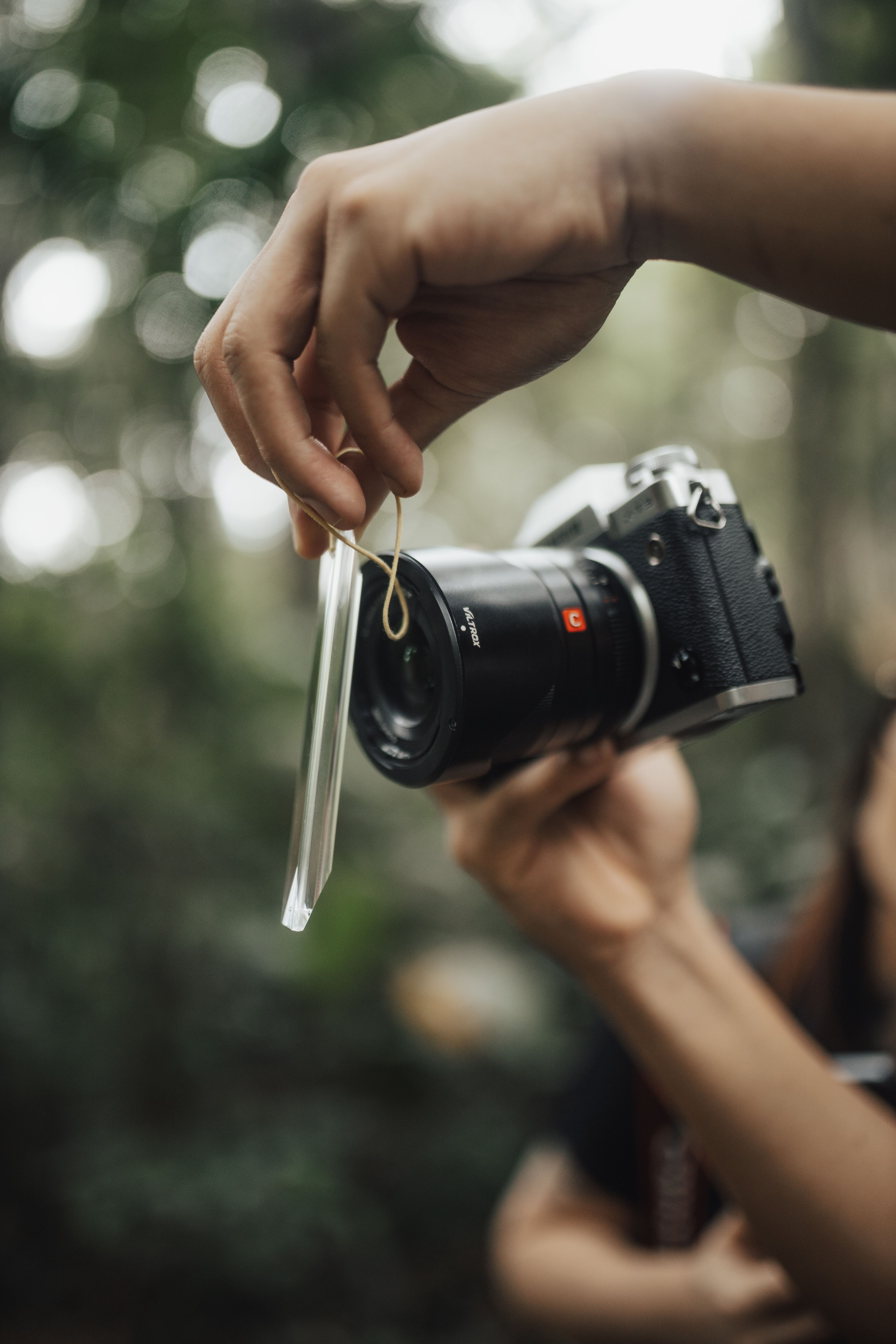 Hands attaching filter to camera lens, outdoor setting, greenery background.