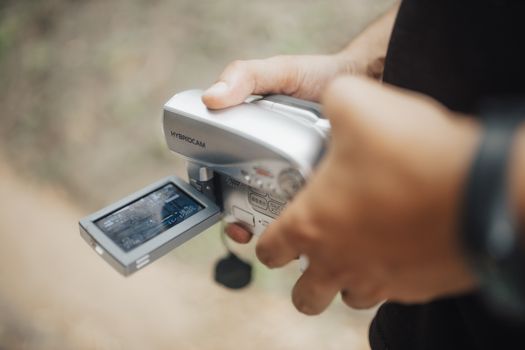 A person holding a hybrid camcorder, capturing a video with an outdoor background.