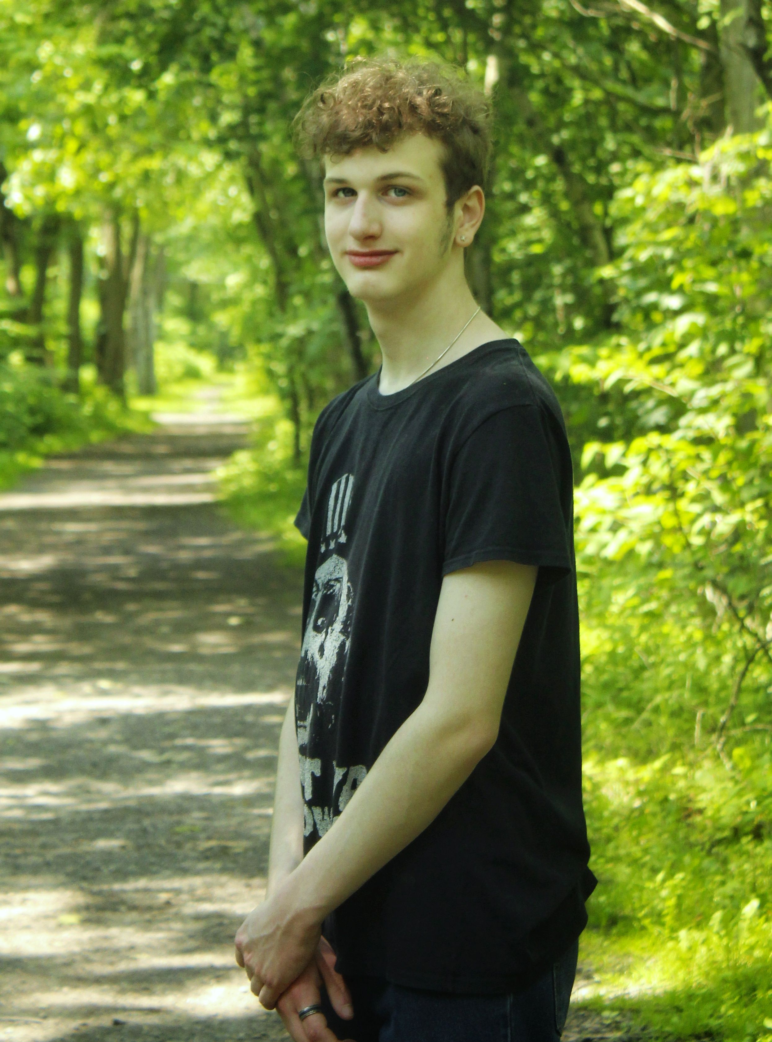 Young male posing on a sunny forest path, capturing nature's lush greenery.