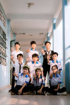 Eight students in uniform pose showing five fingers each in a bright hallway.