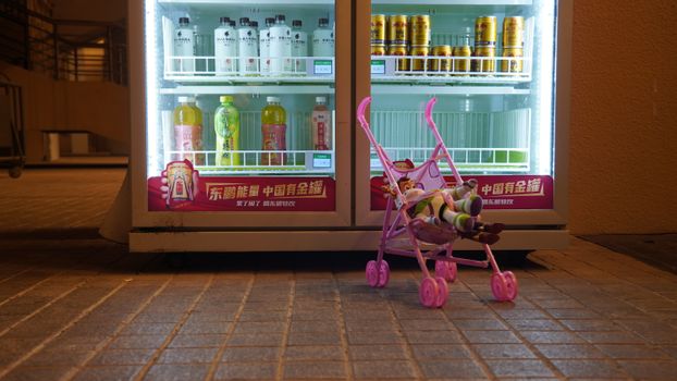 A child's toy stroller with a doll in front of a vending machine at night.