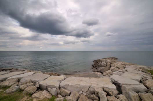 Panoramic view of a rocky seascape with dramatic clouds and calm waters evokes a moody coastal atmosphere.