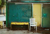 Outdoor scene featuring an empty white plastic chair and weathered metal grid in Buenos Aires.