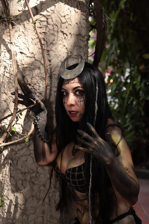 Free Intriguing woman with elaborate makeup and accessories posing outdoors against a textured wall. Stock Photo