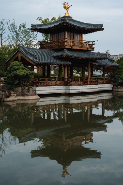 Free Serene image of an Asian pavilion with reflection in a calm pond, surrounded by lush greenery. Stock Photo