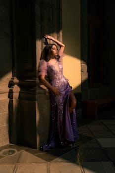 Model in a stunning purple gown standing in artistic shadow and light.